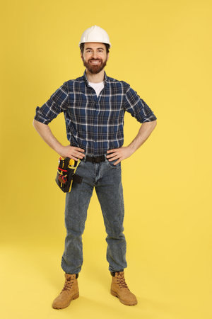 Professional builder with tool belt on yellow backgroundの写真素材