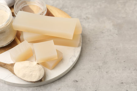 Gelatin powder in spoon and jelly pieces on gray textured table, closeup.の写真素材