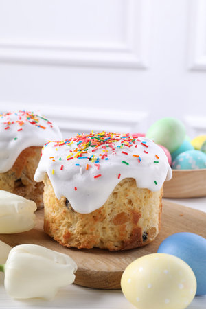 Delicious Easter cakes, painted eggs and tulips on white wooden table, closeup