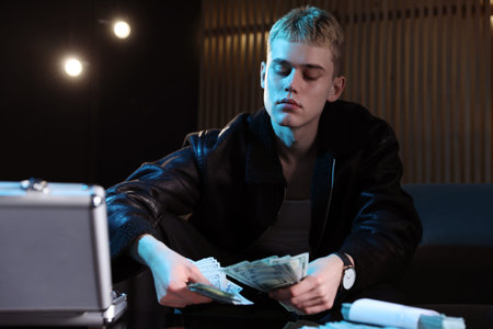 Young businessman in jacket with dollar banknotes in dark room