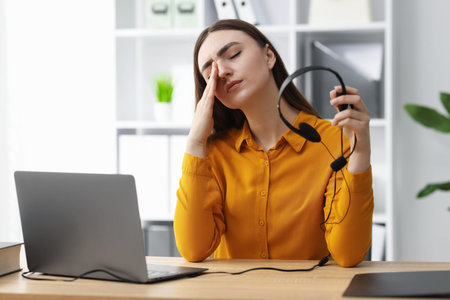 Work fatigue. Overwhelmed businesswoman with headset suffering at table in officeの写真素材