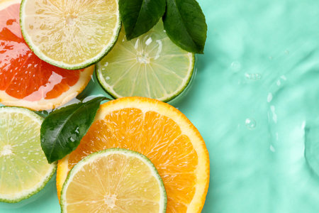 Slices of citrus fruits and green leaves in water on turquoise background, flat lay. Space for textの写真素材