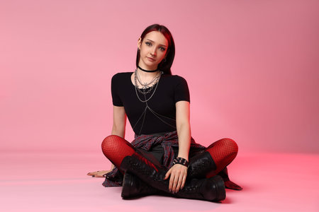 Young woman with piercings posing in red light on pink backgroundの写真素材