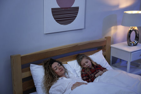 Mother and daughter sleeping with illuminated night lamp at homeの写真素材