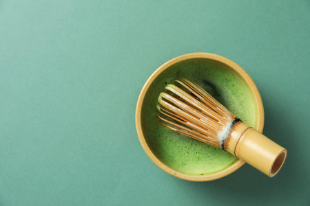 Refreshing green matcha in ceramic bowl and bamboo whisk on green table, top view. Space for textの写真素材