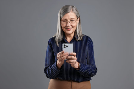 Beautiful senior woman with smartphone on gray background