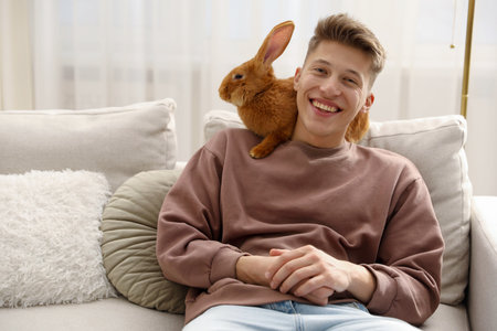 Happy man with cute bunny on sofa at homeの写真素材