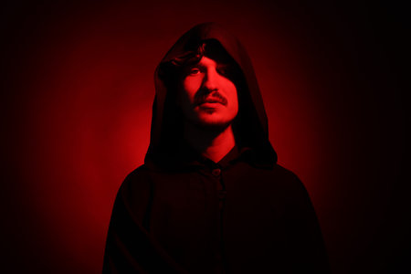 Man in hood on dark background with red light