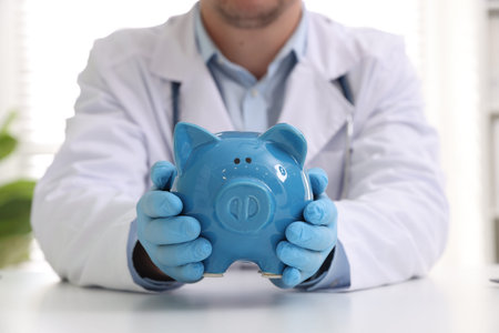 Doctor with piggy bank at white table indoors, closeupの写真素材