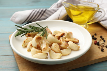 Grilled garlic cloves with spices on light blue wooden table, closeup