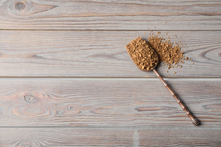 Pile of instant coffee and metal scoop on wooden table, top view. Space for text