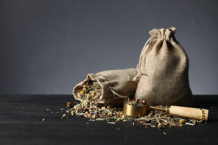 Burlap sacks with dried herbal tea leaves and scoop on black wooden table against gray background. Space for textの写真素材