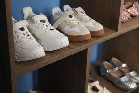 Different stylish children's shoes on wooden shelving unit indoors, closeupの写真素材