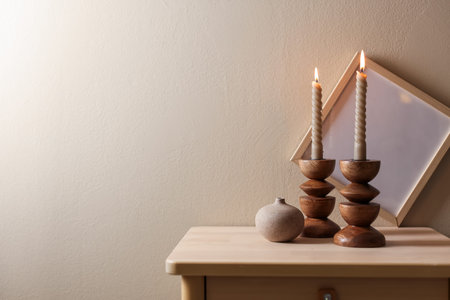 Beautiful burning candles in candlesticks, frame and decor on wooden table near beige wall. Space for textの写真素材