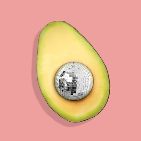 Avocado half with disco ball instead of seeds on pink background