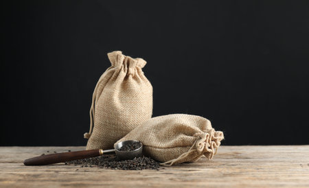 Dried black tea leaves, burlap sacks and scoop on wooden table against dark backgroundの写真素材