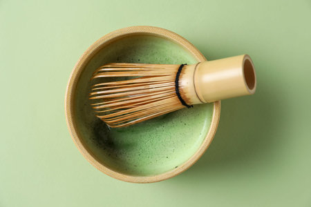 Refreshing green matcha in ceramic bowl and bamboo whisk on green table, top view