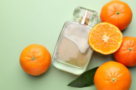 Bottle of perfume and tangerines on light green background, flat lay. Space for text