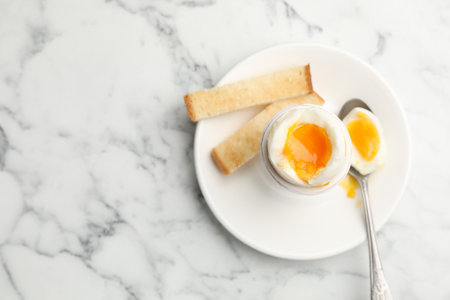 Tasty breakfast with soft boiled egg and toasted bread on white marble table, top view. Space for...