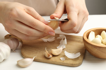 Woman peeling fresh garlic at white wooden table, closeupの写真素材