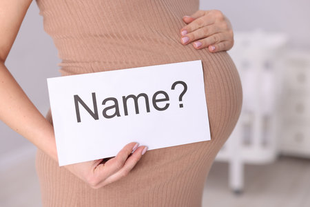 Pregnant woman holding card with word Name and question mark indoorsの写真素材