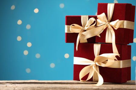 Beautiful velvet gift boxes on wooden table against light blue background with bokeh lights,...