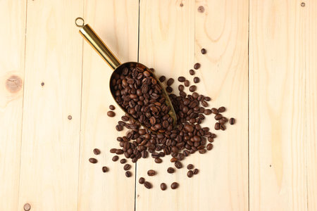 Pile of coffee beans and metal scoop on light wooden table, top viewの写真素材