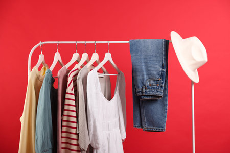 Different clothes and hat hanging on rack against red backgroundの写真素材