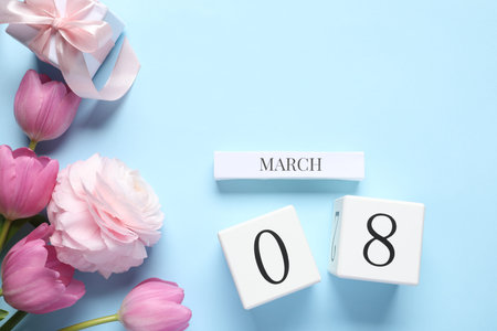 Gift box, wooden block calendar and beautiful flowers on light blue background, flat lay
