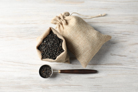 Dried black tea leaves in burlap sacks and scoop on wooden table, flat layの写真素材