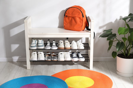 Shoe storage bench with different children's footwear, backpack and houseplant indoorsの写真素材