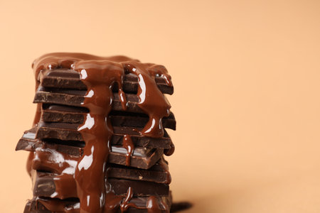 Pieces of chocolate melting on beige background, closeup. Space for text