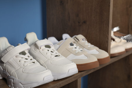 Different stylish children's shoes on wooden shelving unit indoors, closeupの写真素材