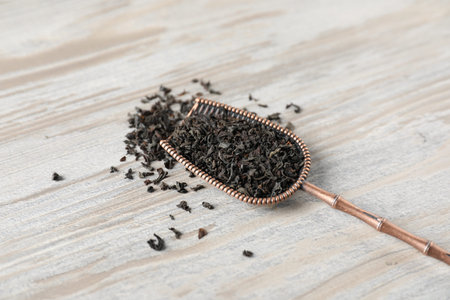 Dried black tea leaves in bronze scoop on wooden table, closeup