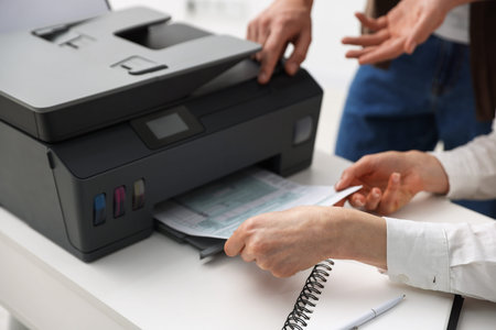 Office workers using printer at white desk indoors, closeup