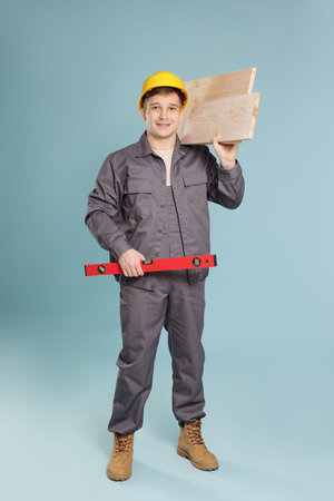 Professional builder with level tool and wooden planks on light blue background