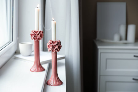 Elegant candlesticks with burning candles on windowsill indoors, space for textの写真素材