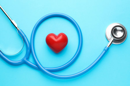 Stethoscope and heart model on light blue background, top view
