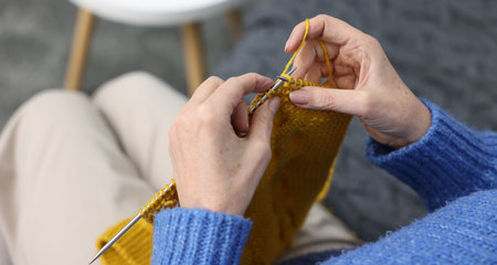 Senior woman knitting with needles on sofa at home, above view