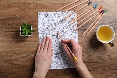 Woman coloring antistress picture with pencils at wooden table, top viewの写真素材