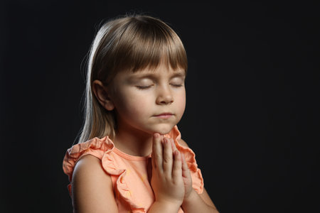 Little girl praying on black background, space for textの写真素材