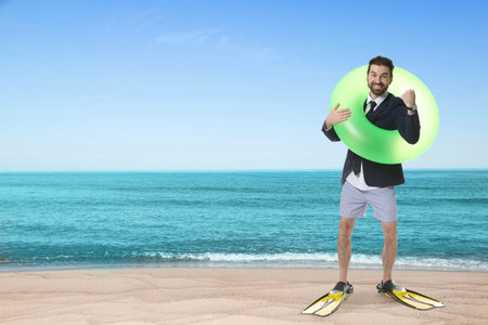 Businessman in formal clothes, swim trunks and fins with swim ring on beach. Time for vacationの写真素材