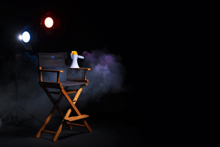 Film director's chair, megaphone and lighting equipment on black background with smoke, space for textの写真素材