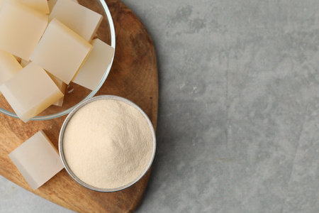 Gelatin powder and jelly cubes in bowl on gray textured table, top view. Space for textの写真素材