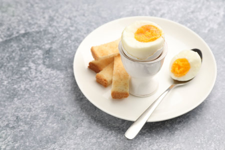 Tasty breakfast with hard boiled egg and toasted bread on gray table, closeup. Space for text