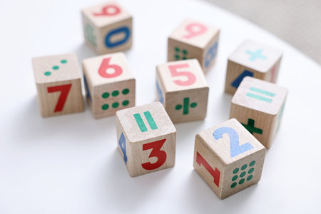 Wooden cubes with numbers and symbols on white table, closeup