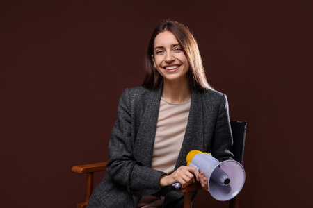 Professional film director with megaphone on chair against brown background. Space for textの写真素材