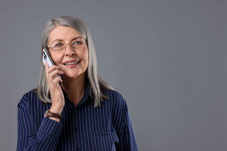 Beautiful senior woman talking on phone against gray background. Space for text