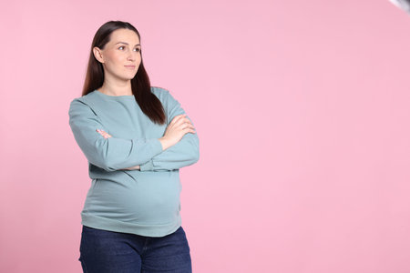 Choosing name for baby. Thoughtful pregnant woman on pink background, space for text