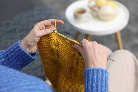 Senior woman knitting with needles on sofa at home, above view